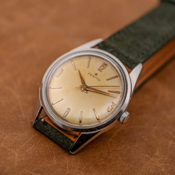 Zenith side-lit dial view with star emblem, applied quarter-hour numerals and forest green suede strap