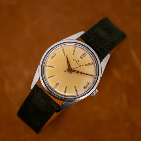 Zenith upright three-quarter portrait with Arabic numerals and forest green suede strap looped beneath the case
