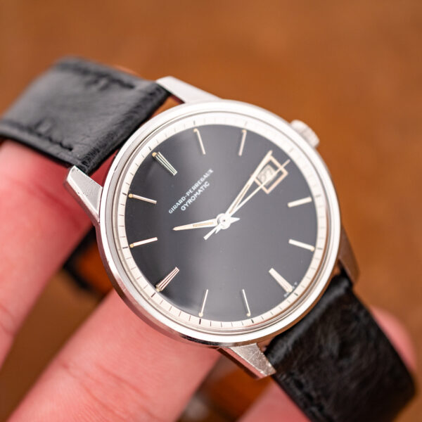 Girard Perregaux Gyromatic held at an angle, displaying black dial and contrasting outer minute track