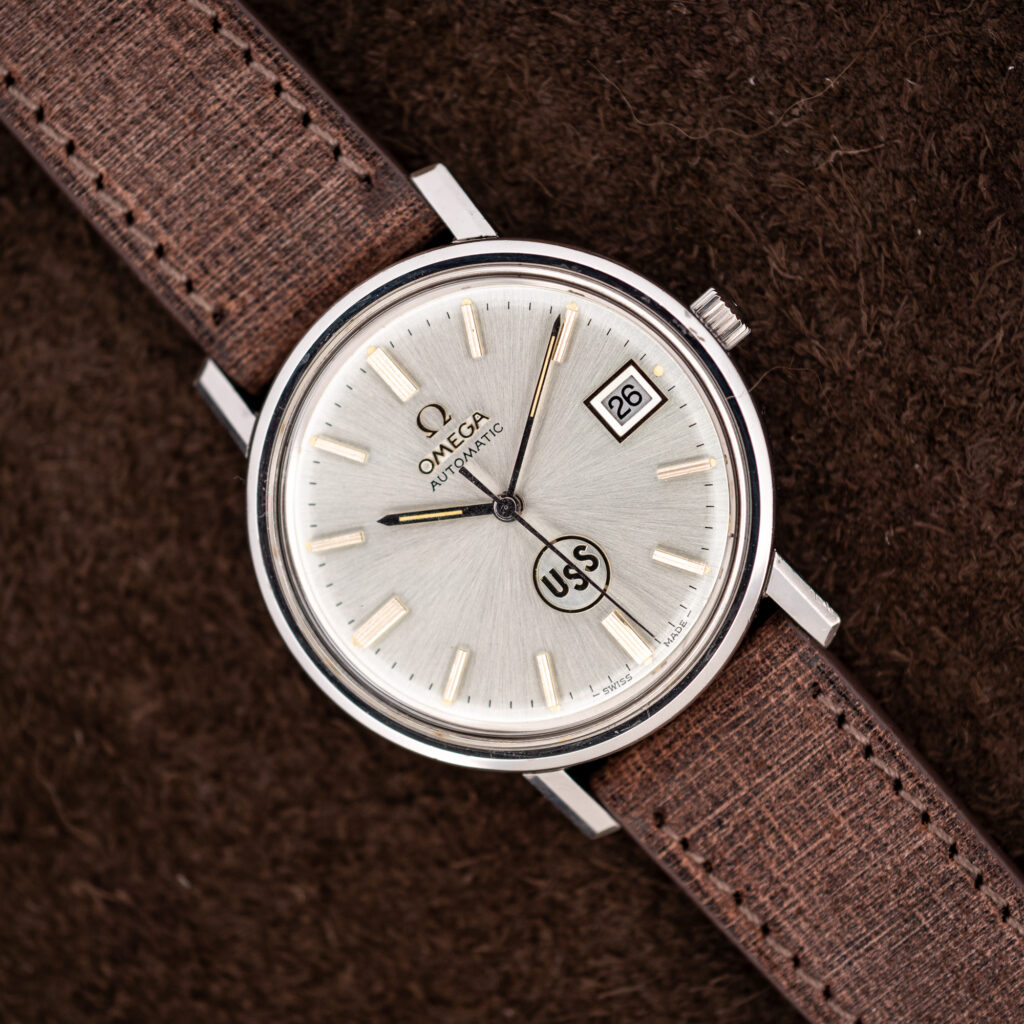 Omega automatic watch diagonal portrait with silver sunburst dial, circular USS emblem and framed date display