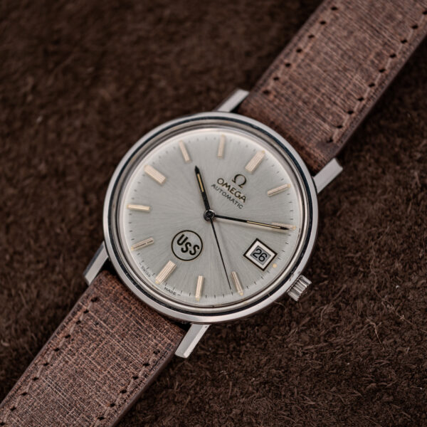 Omega automatic watch wide diagonal arrangement with silver sunburst dial and stitched strap extending on both sides