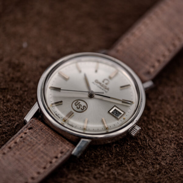Omega automatic crown-side angle with circular USS emblem, date display and silver sunburst dial texture