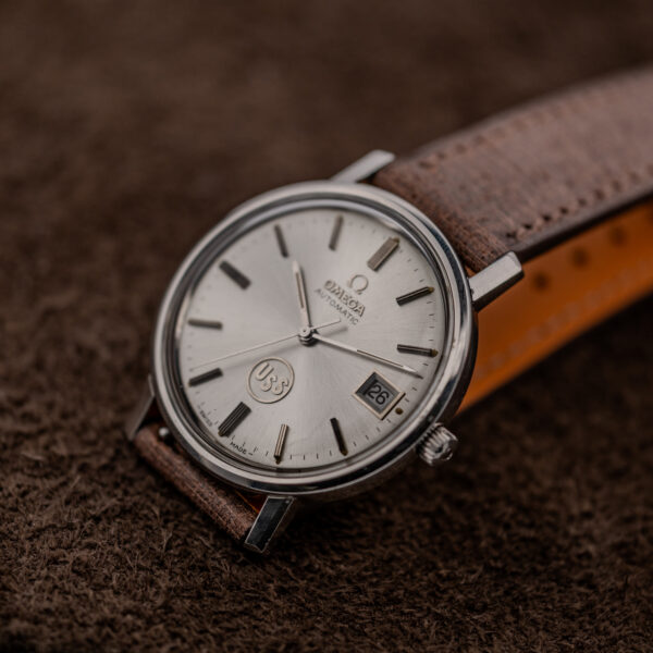 Omega automatic near-frontal portrait with circular USS emblem, silver sunburst dial and framed date aperture