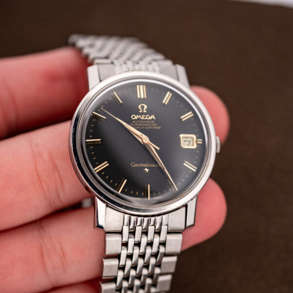 Omega Constellation 168.010 held in a hand with black dial, applied star and draped bracelet