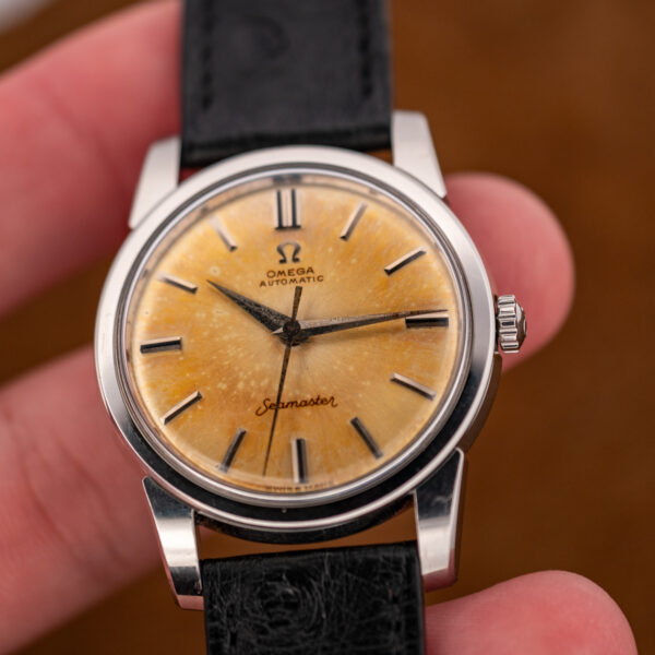 Close hand-held view of the amber Omega Seamaster dial with broad pointed hands and applied markers