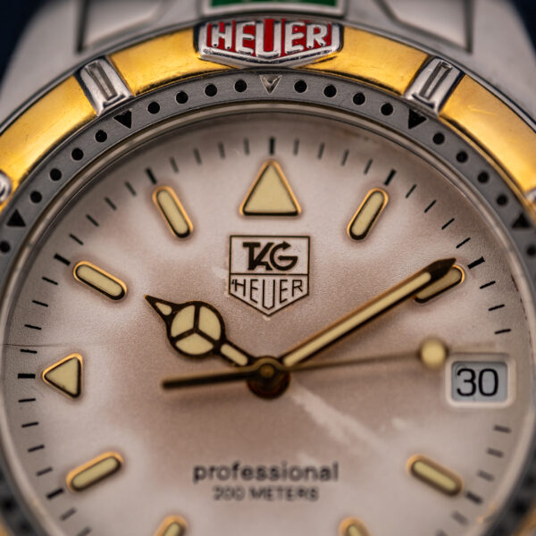 Upper half of the TAG Heuer 995.706 K dial with the shield logo, pale hour markers and timing bezel