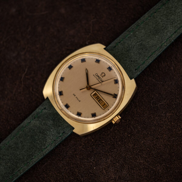 Omega De Ville 166.053 face-on with the forest green suede strap laid out at full length
