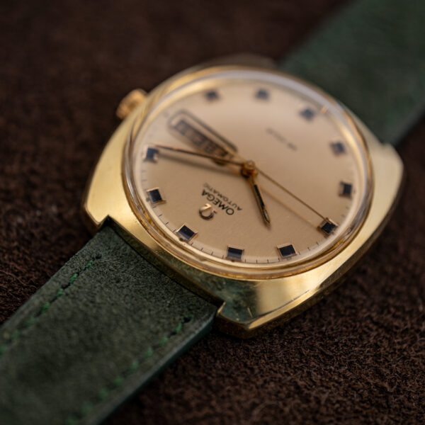 Omega De Ville day-date watch photographed upside down at a low angle, showing dial and green suede strap