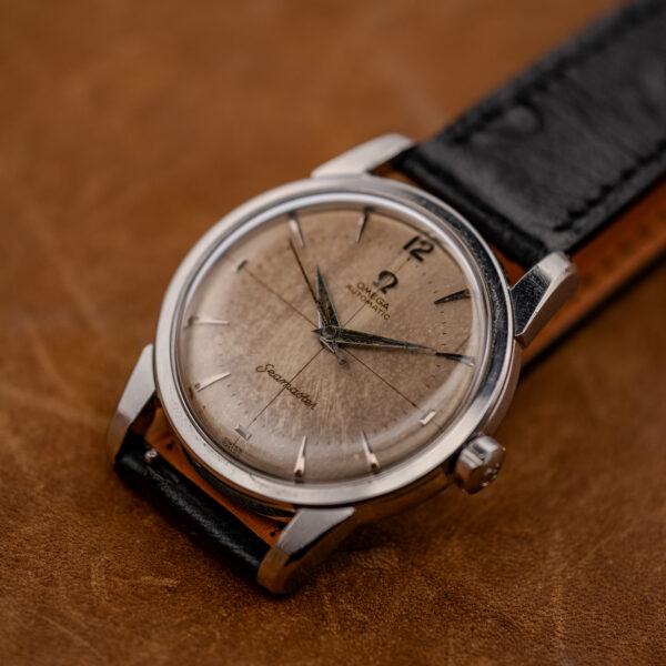 Low crown-side view of the Omega Seamaster showing the patina crosshair dial and black textured strap
