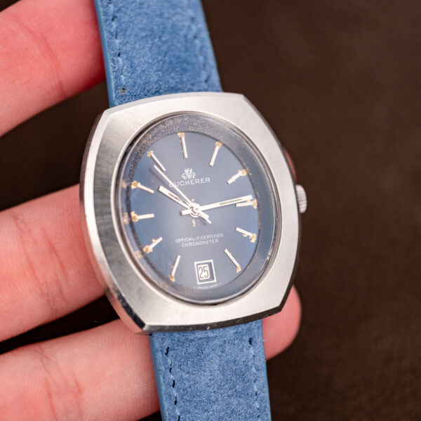 Handheld angled view of the Bucherer chronometer with date at six and blue suede strap