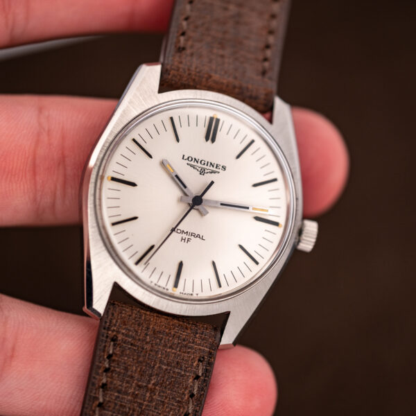 Close handheld view of the Longines Admiral HF dial, baton hands and yellow-toned plots at the quarters