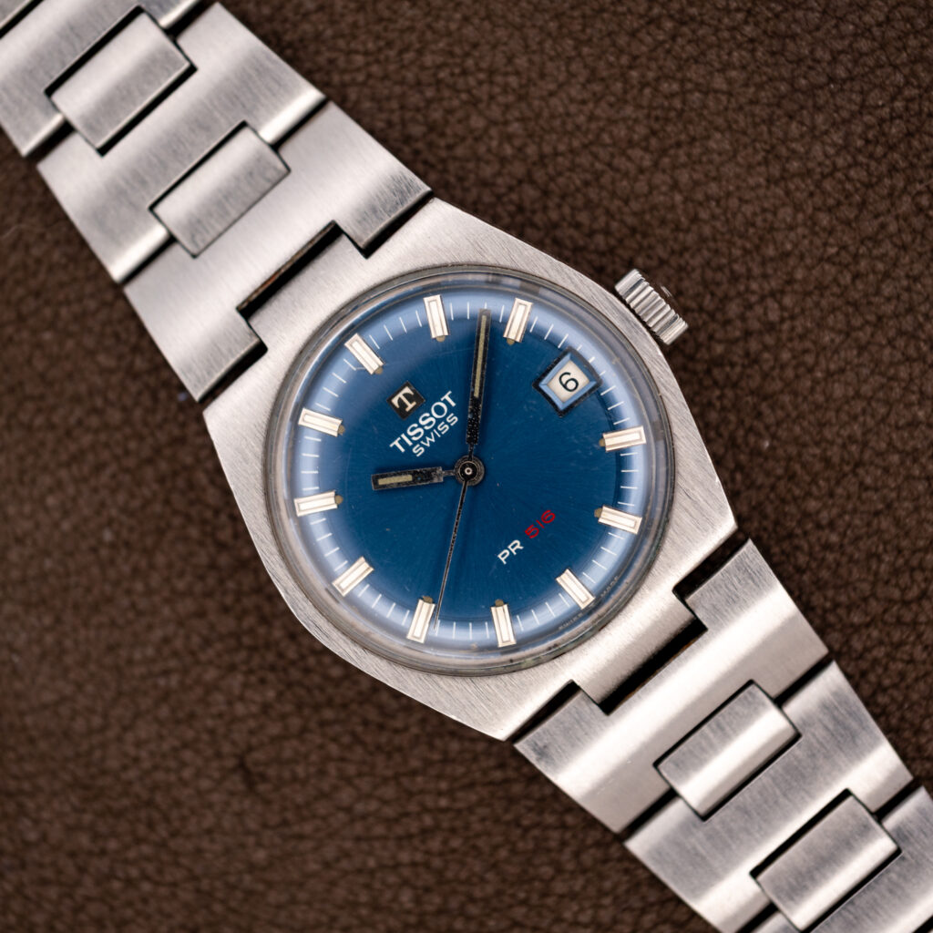 Vintage Tissot PR 516 at a diagonal with blue dial, red 516 lettering, date window and steel bracelet
