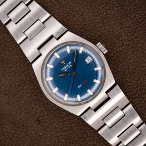 Vintage Tissot PR 516 at a diagonal with blue dial, red 516 lettering, date window and steel bracelet