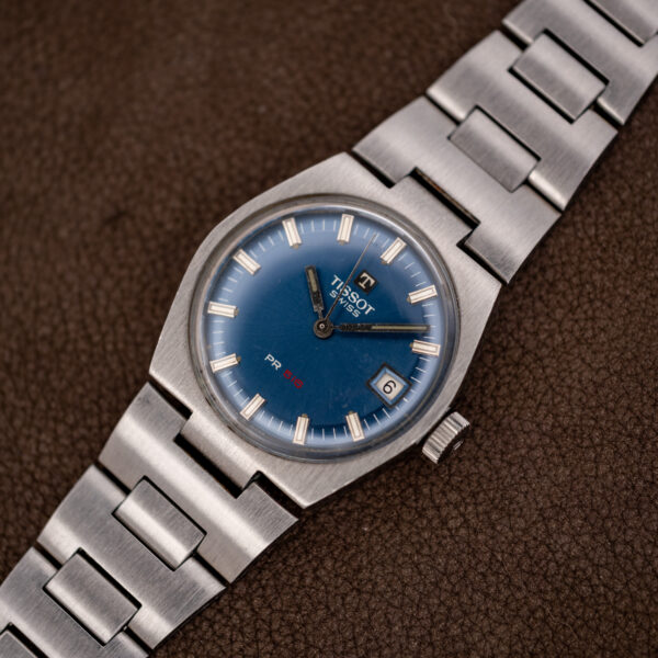Tissot PR 516 from the opposite angle, showing the radial blue dial and broad steel H-link bracelet
