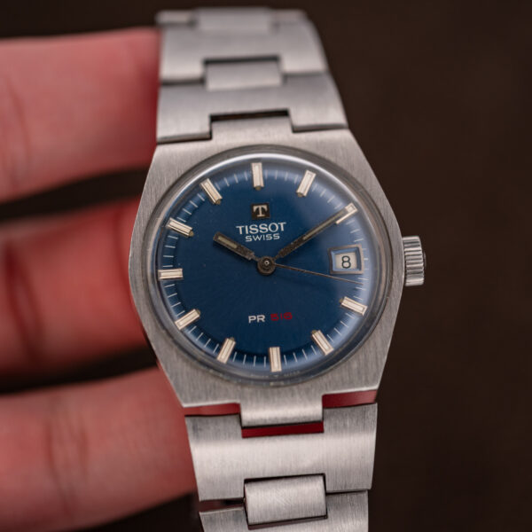 Tissot PR 516 held in hand, blue dial with red 516, date at three and steel bracelet