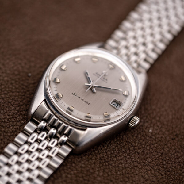 Low crown-side view of the vintage Omega Seamaster showing the silver dial, date aperture and tonneau case