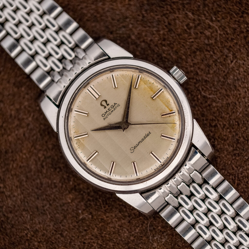 Omega Seamaster 165.009 ribbon dial seen from above on a silver multi-row beads-of-rice bracelet