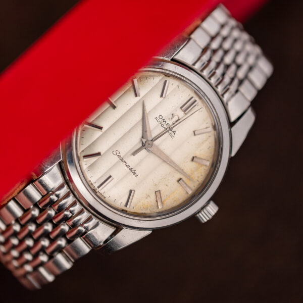 Oblique view of the Omega Seamaster ribbon dial with the upper-left edge hidden by a red support