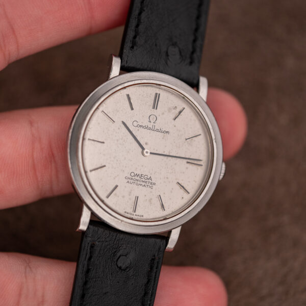 Omega Constellation 157.0001 held in hand under diffuse light, flecked silver dial and black ostrich strap