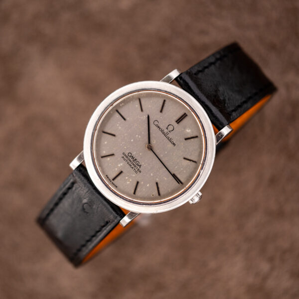 Omega Constellation automatic chronometer on a round stand with its strap curved, dial showing scattered flecks