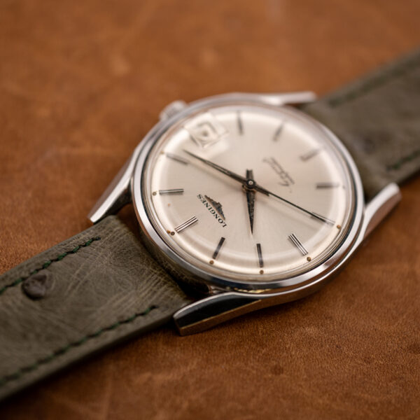 Opposite low oblique view of the Longines Conquest 7171-2 dial and steel case on olive ostrich