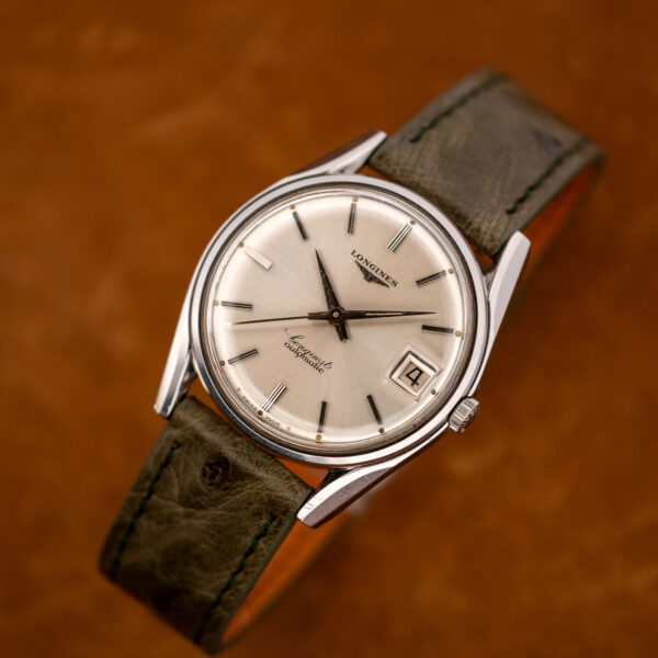 Raised three-quarter view of the Longines Conquest 7171-2 showing the steel case, silver dial and olive strap