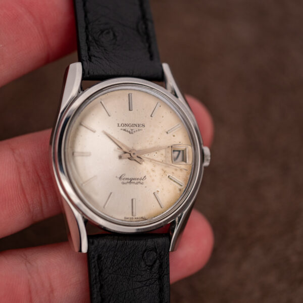 Longines Conquest 7171-5 held in hand, spotted silver dial and black strap facing the camera
