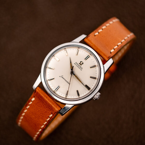 Raised front view of the white-dial Omega Seamaster with its tan strap looped behind the case