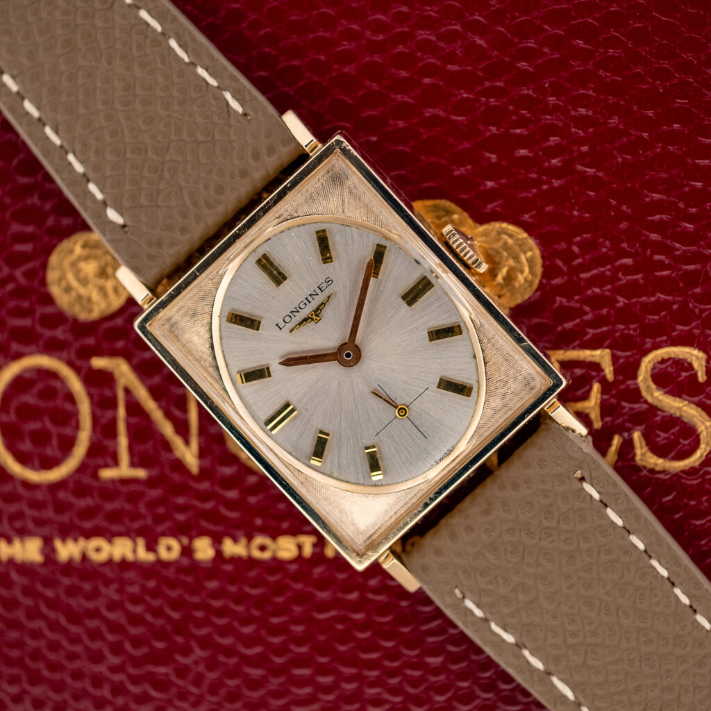 Longines 1137-370 tank on a red Longines box, angled to show the oval silver dial and taupe strap