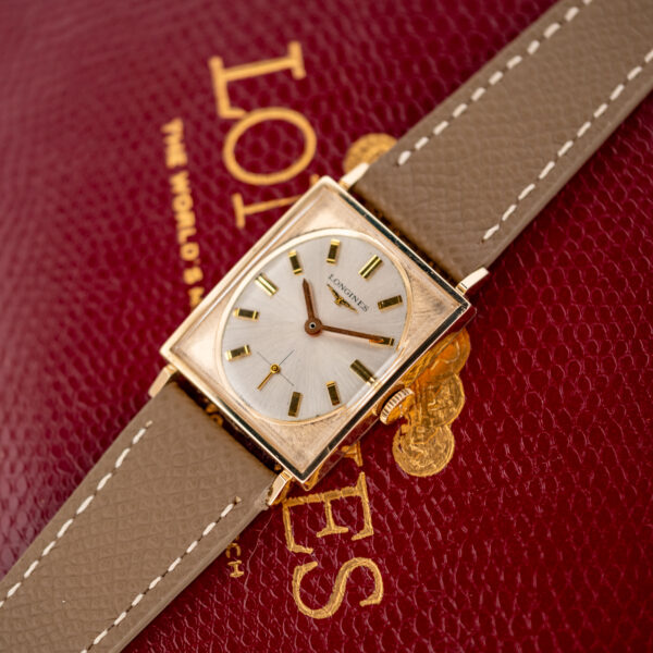 Longines 1137 gold-filled tank on a red box, seen from the opposite angle with its taupe leather strap