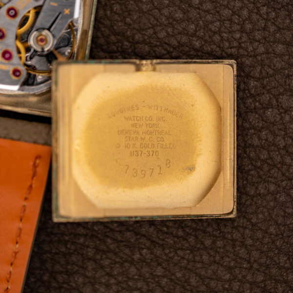 Removed inner caseback of the Longines 1137-370 with its stamped lettering, beside the open case and movement