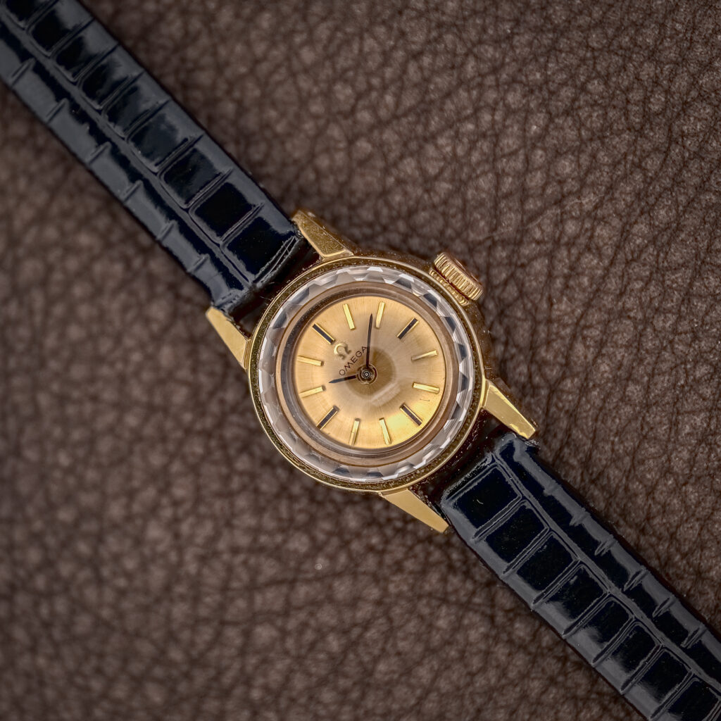 Omega 511.166 ladies watch at a diagonal, faceted crystal over the champagne dial and black strap