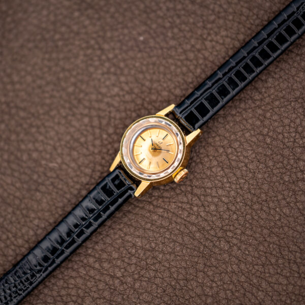 Full-length diagonal view of the vintage Omega ladies watch on its black glossy patterned strap