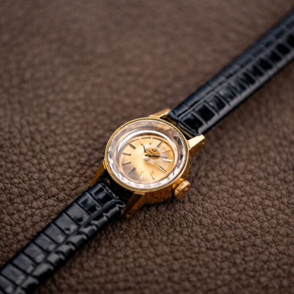 Low crown-side angle of the Omega 511.166 showing the raised faceted crystal and gold-tone bezel