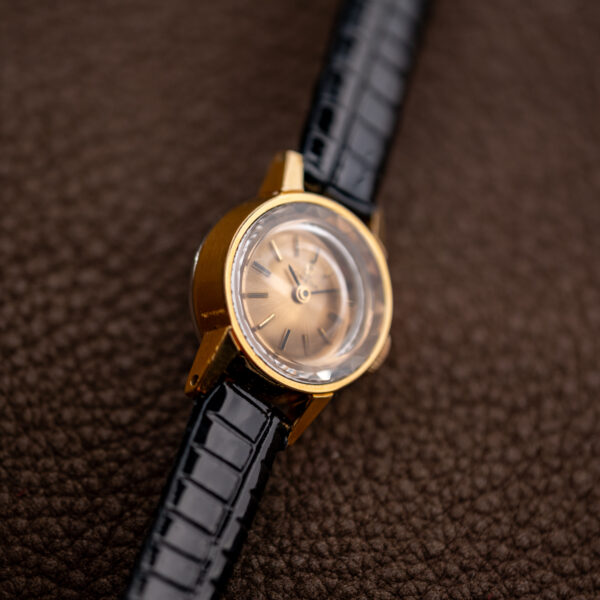 Omega ladies cocktail watch from a low left angle, faceted crystal edge catching light over the dial
