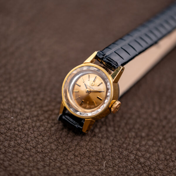Three-quarter view of the Omega 511.166 faceted crystal, signed crown and champagne dial