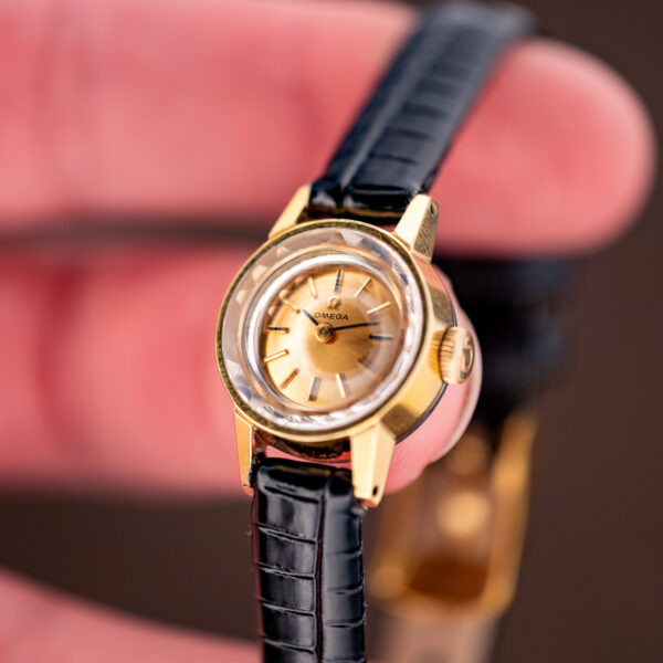 Hand-held crown-side view of the Omega ladies watch, facets ringing the champagne two-hand dial